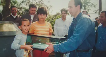 Foto colorida de 1998 mostrando o Rev Dirceu Alves, Murilo Vassão e Aline Muniz na cerimônia com a nova cápsula do tempo, selada em um recipiente de vidro.